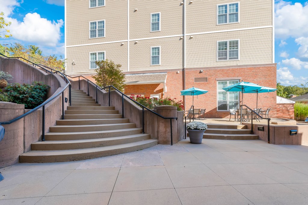 A building with a staircase leading to a patio with a table and chairs.