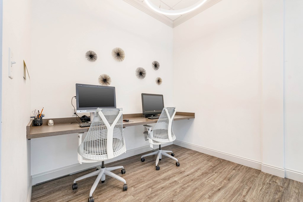Two white chairs are positioned in front of two computers on a desk.