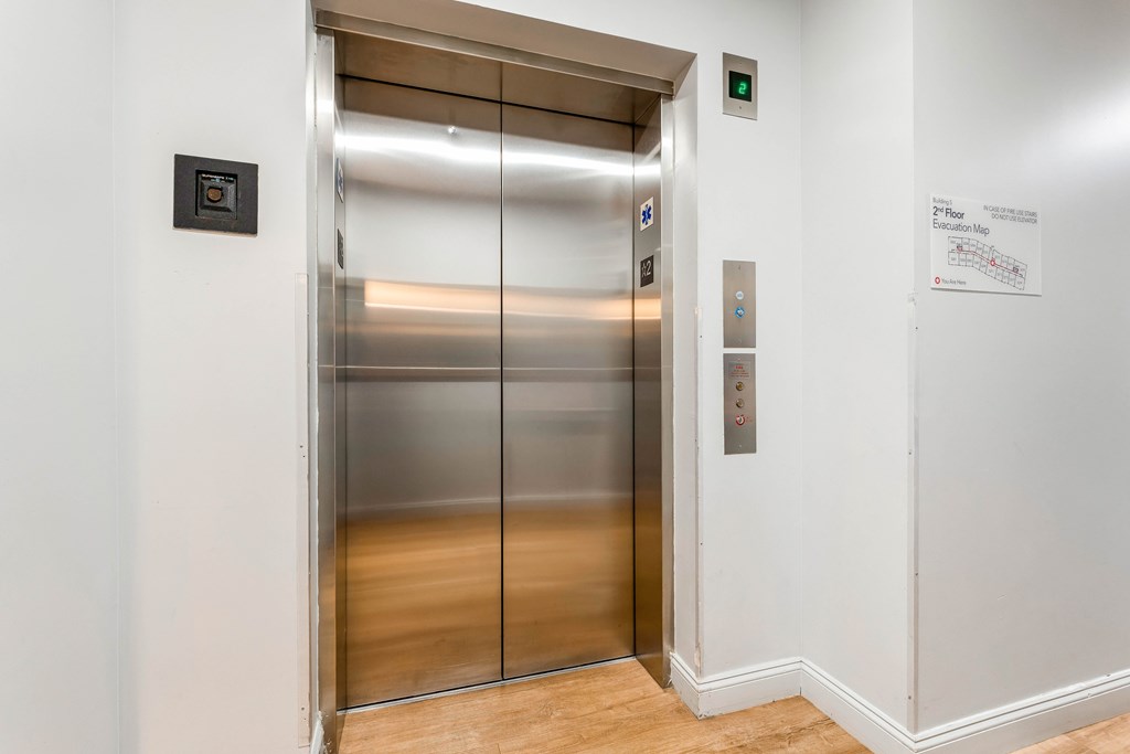 A stainless steel elevator with a glass door and a control panel on the right side.