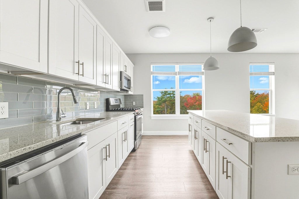 A kitchen with white cabinets and a view of trees through the window.