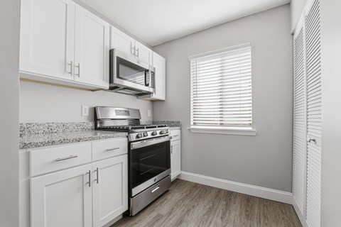 A kitchen with white cabinets and a stainless steel stove and microwave.