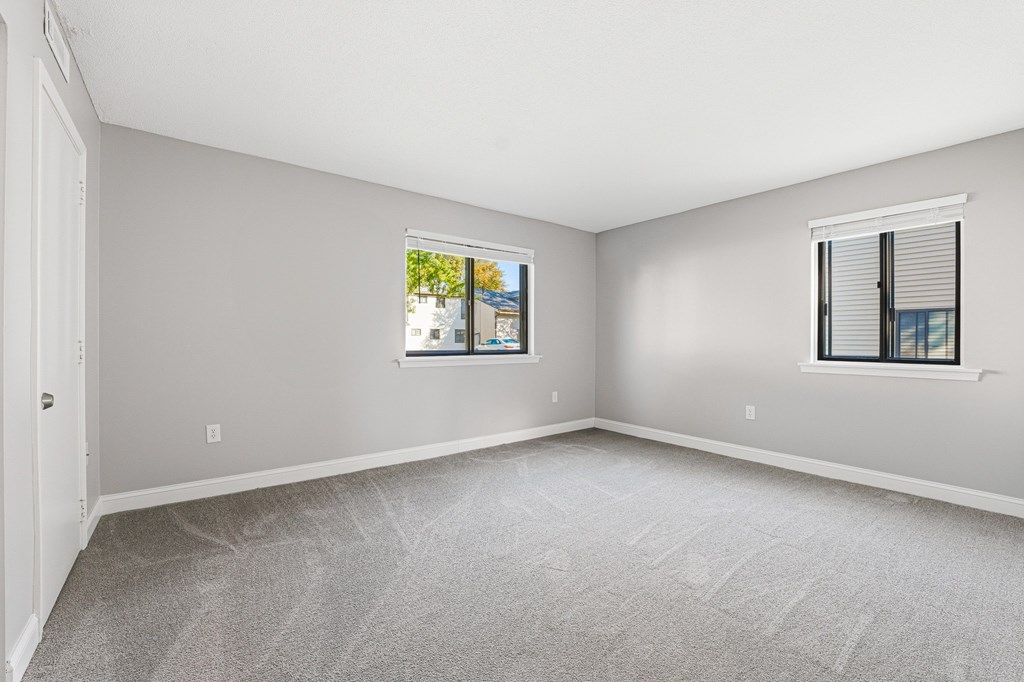 A room with a carpeted floor and two windows. at Hidden Brook Apartment Homes, New Bedford, 02740