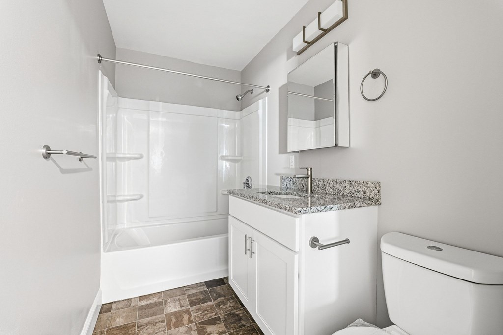 A white bathroom with a marble countertop and a walk-in shower. at Hidden Brook Apartment Homes, Massachusetts, 02740