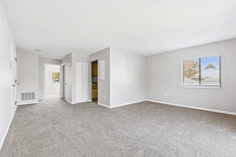 A spacious room with a carpeted floor and a window with blinds.