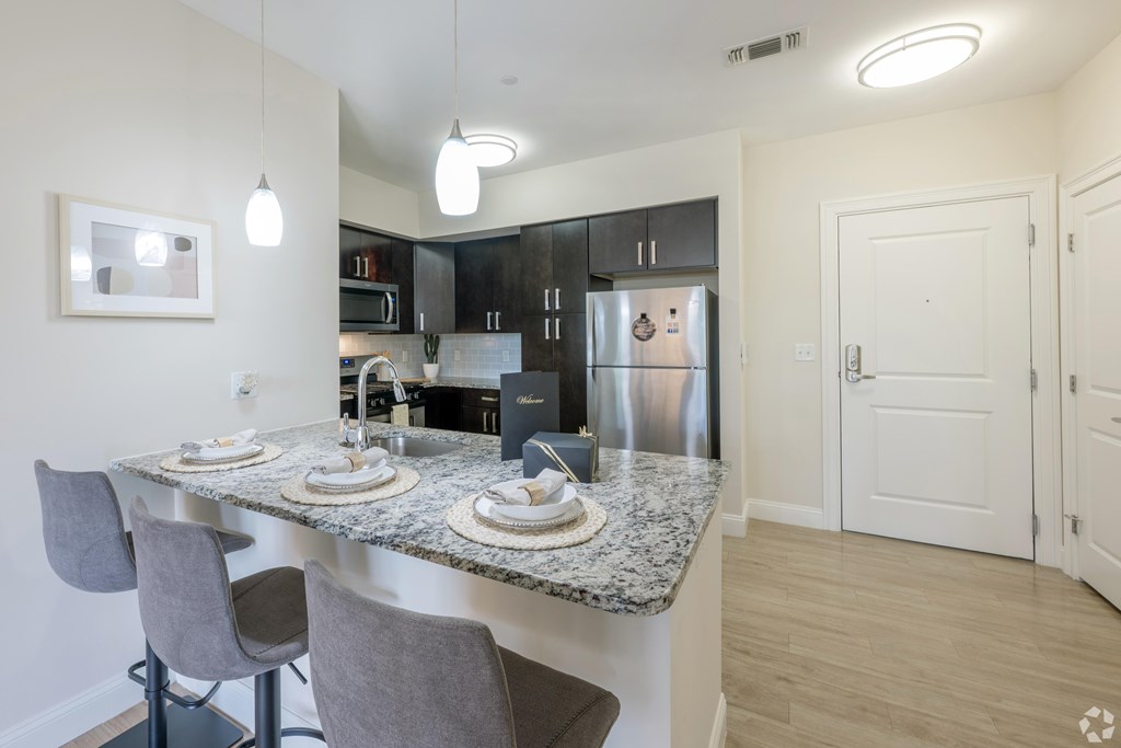 A kitchen with a granite countertop and grey chairs at Axis at Lakeshore Apartments, Bridgewater, Massachusetts