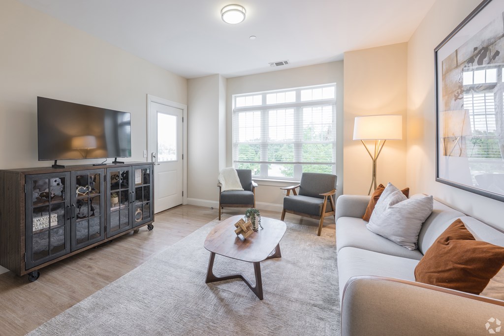 A living room with a grey sofa, a wooden coffee table, and a television at Axis at Lakeshore Apartments, Bridgewater