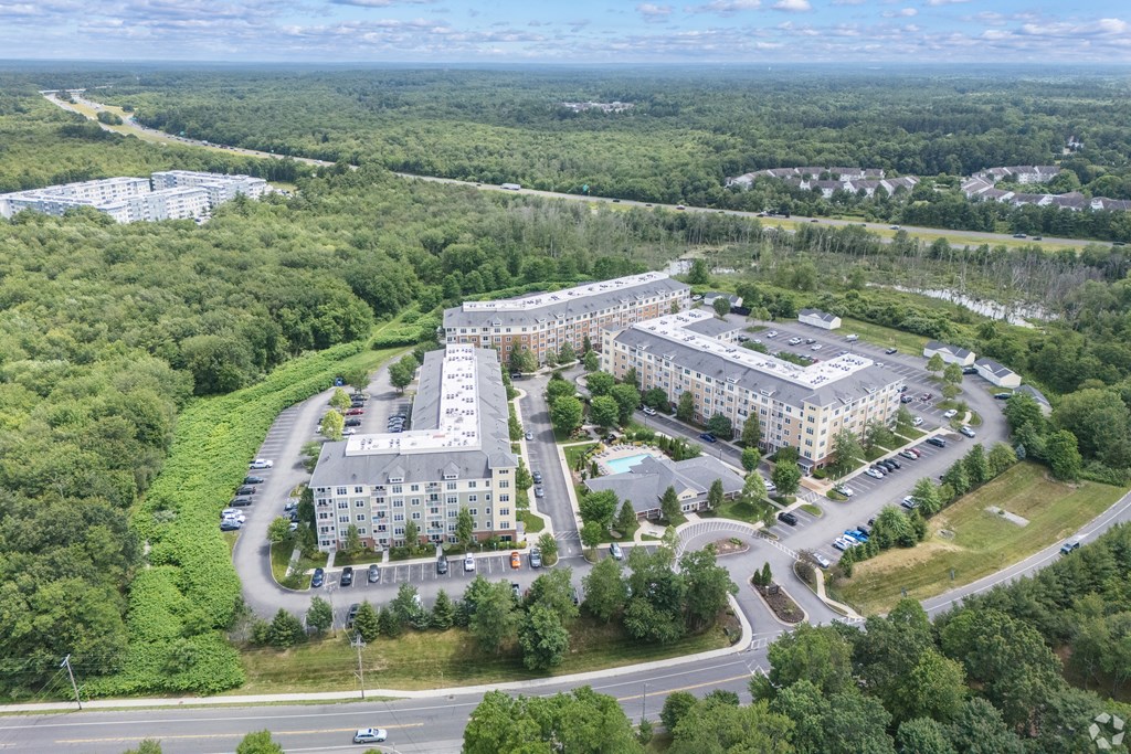 A large building complex surrounded by trees and a parking lot at Axis at Lakeshore Apartments, Bridgewater, MA