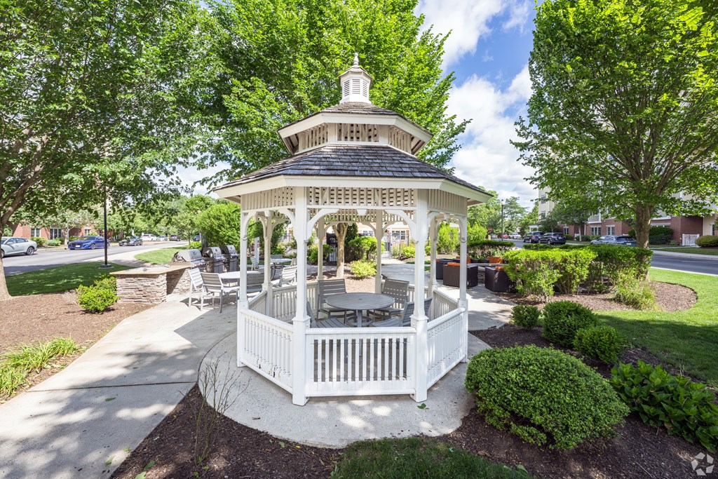 A gazebo with a white railing and a black roof is surrounded by green bushes and trees at Axis at Lakeshore Apartments, Bridgewater, MA