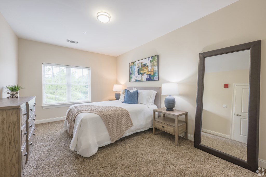 A bedroom with a bed, a nightstand, and a mirror at Axis at Lakeshore Apartments, Bridgewater, MA