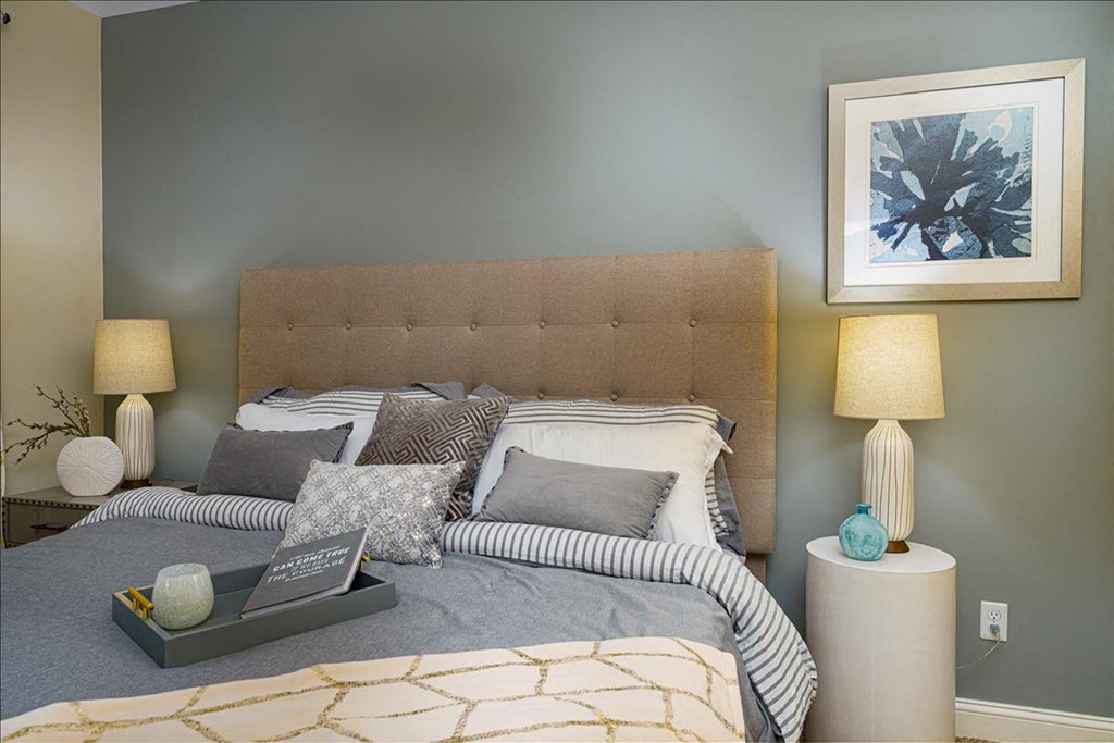 A bed with a grey headboard and a grey blanket with a gold pattern on it at Axis at Lakeshore Apartments, Bridgewater