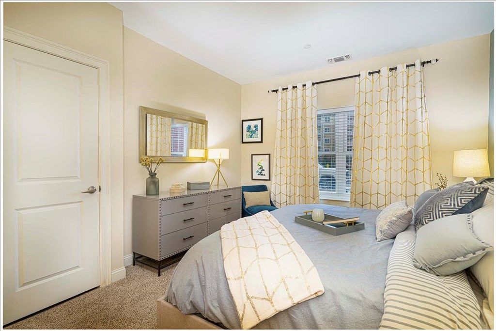 A bedroom with a bed, nightstand, and a window with curtains at Axis at Lakeshore Apartments, Massachusetts