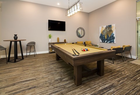 A room with a pool table and a television on the wall.