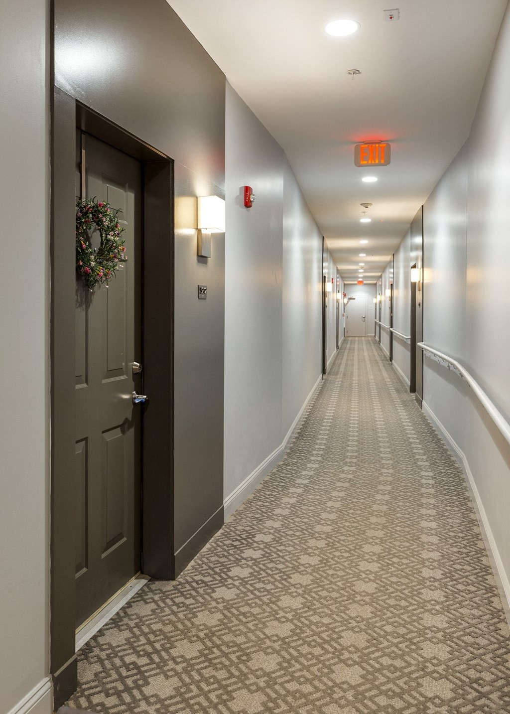 a hallway with gray walls and a tiled floor and a dark door