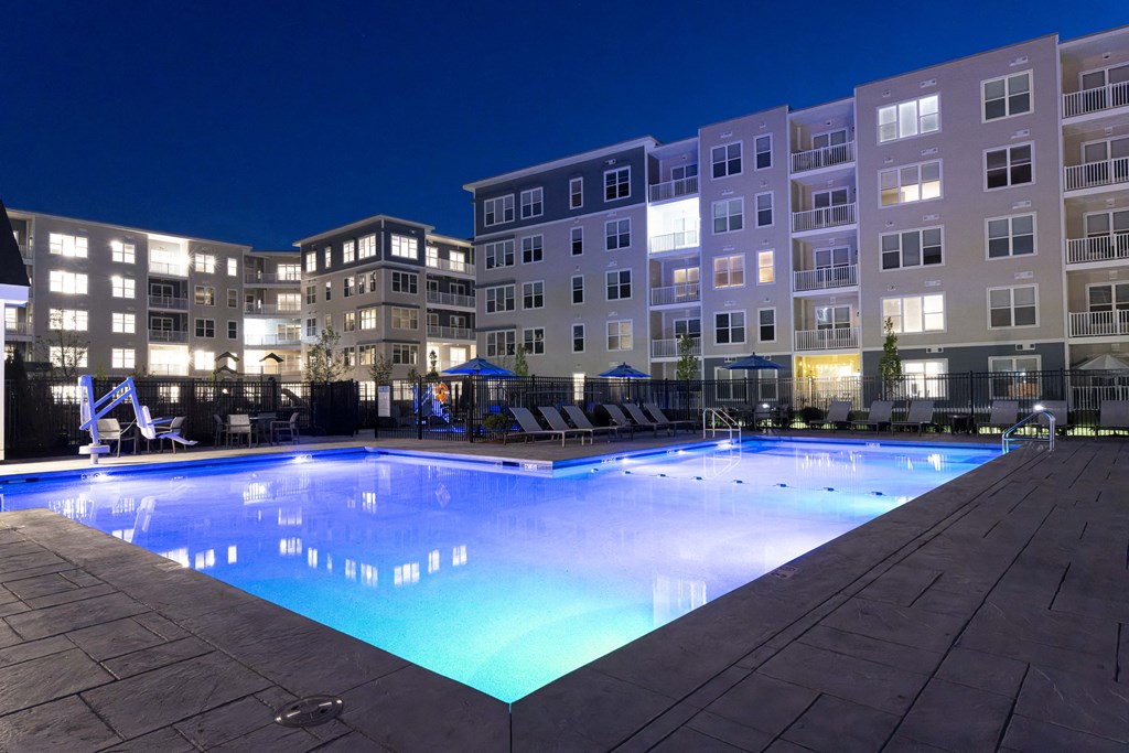 a swimming pool at night with an apartment building in the background