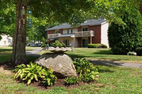 A large rock in the middle of a garden with a house in the background.