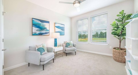 A living room with two grey couches, a ceiling fan, and two paintings on the wall.