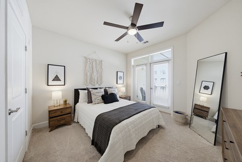 Carpeted bedroom with a ceiling fan, two nightstands, a tall leaning floor mirror, and a balcony door with blinds.