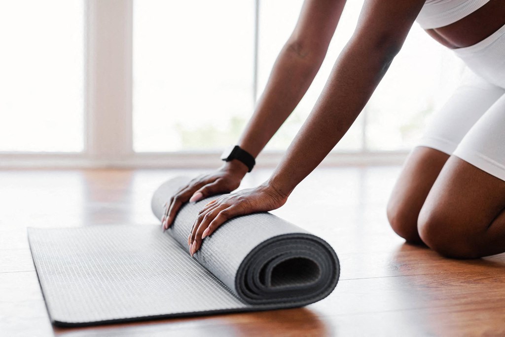 a woman rolls up a yoga mat on the floor