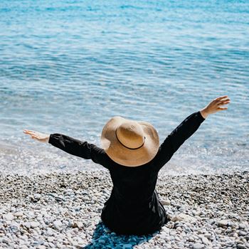 a woman sitting on the beach with her arms outstretched