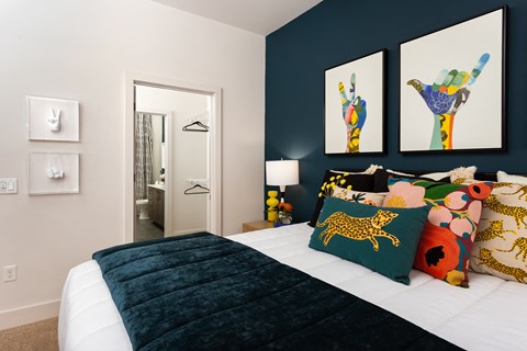 Bedroom with layered pillows and a velvet throw, opening through a doorway to the attached bathroom and closet.