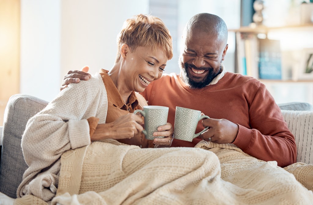 a man and a woman sitting on a couch laughing and holding coffee cups
