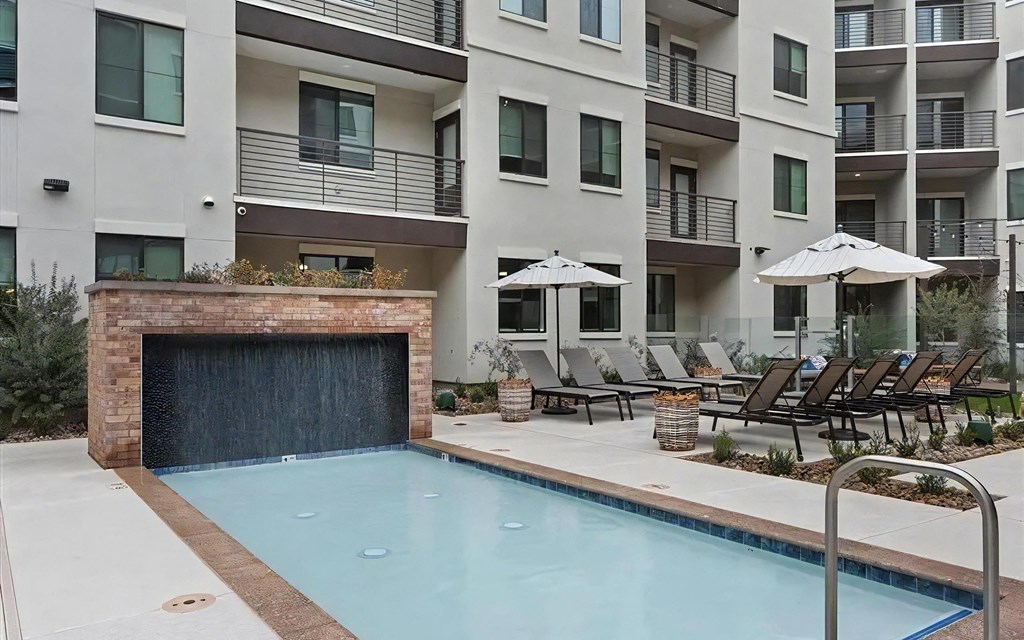 a swimming pool with chairs and umbrellas in front of an apartment building