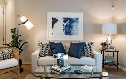 Seating area with a cream sofa, navy pillows, a large framed print, and a round side table with a ceramic lamp.