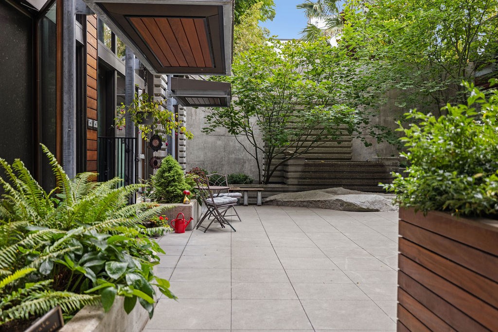 A patio with a table and chairs surrounded by green plants.