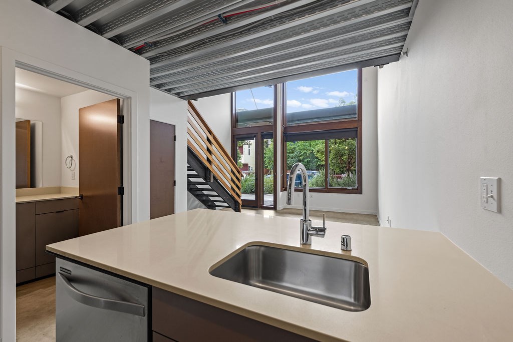 A kitchen with a stainless steel sink and a window overlooking a staircase.
