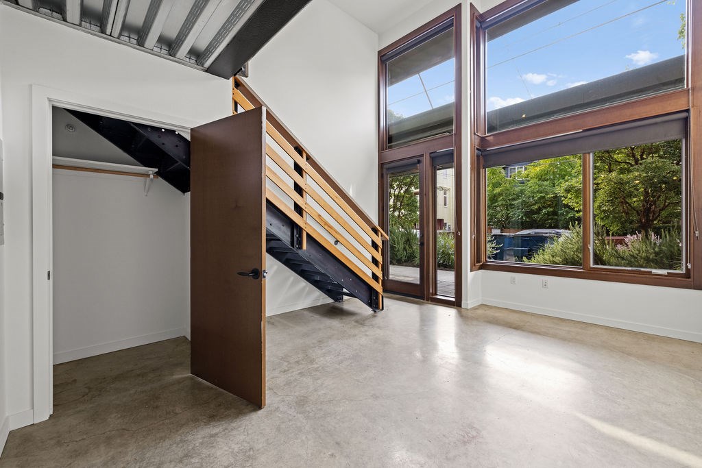A room with a wooden door and a window with a view of trees and a car outside.