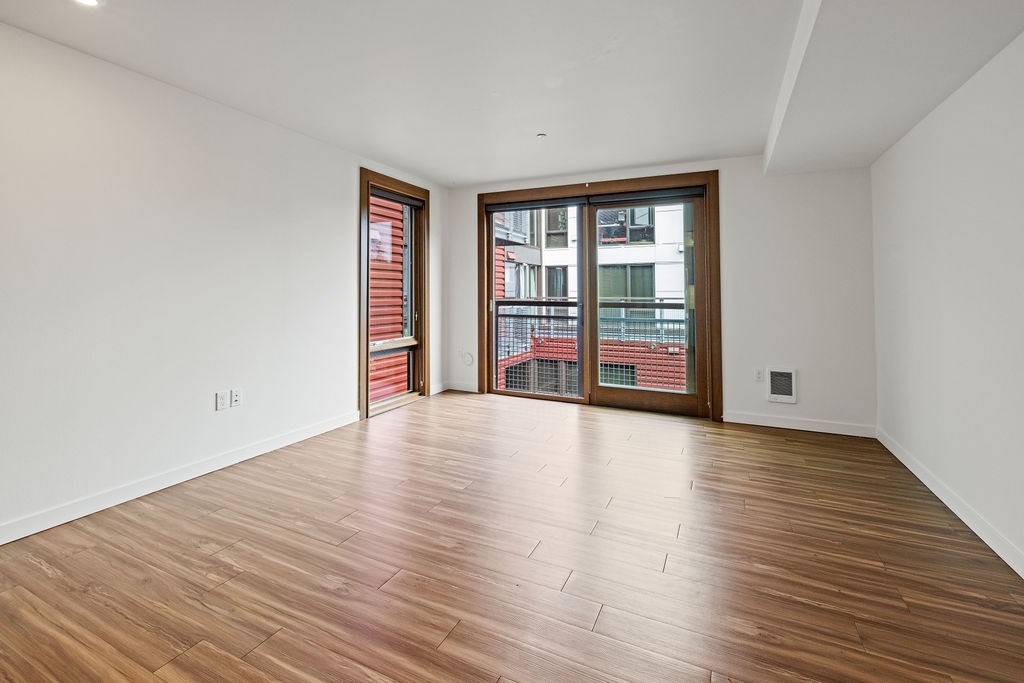 A room with wooden flooring and a large window with a view of a cityscape.