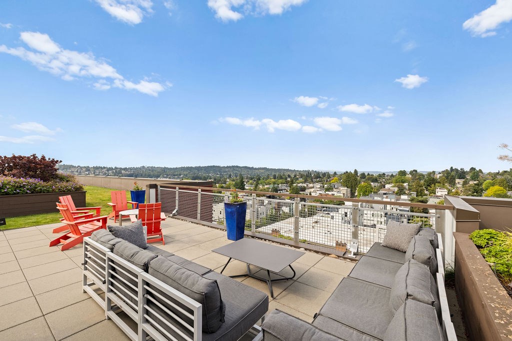 A patio with grey couches and red chairs overlooks a cityscape.