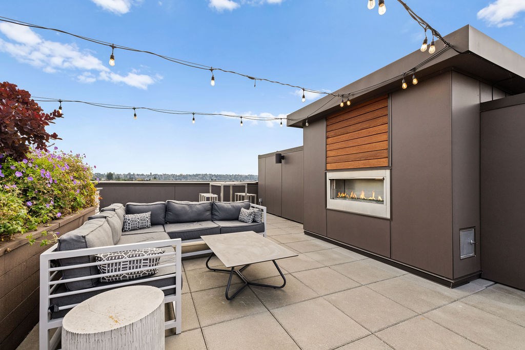 A modern patio with a grey couch, a white table, and a fireplace.