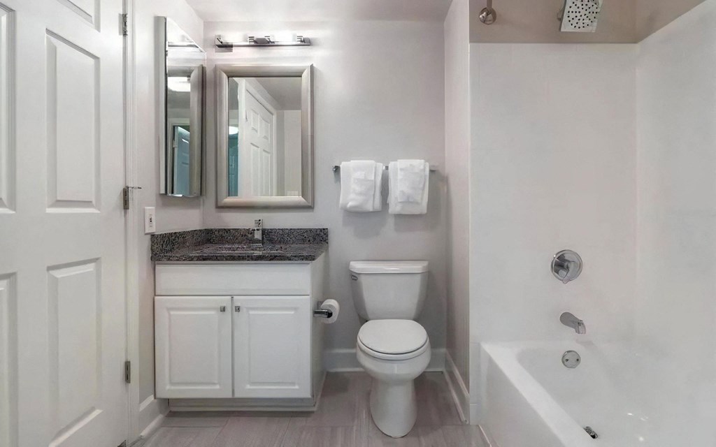 White-Tiled Bathtub and Sink Area With Framed Mirror and Granite Counter