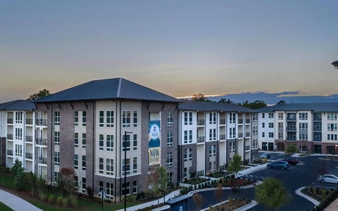 Broadstone Trailside apartment buildings at dusk, four stories in brick and siding, with surface parking and landscaping.