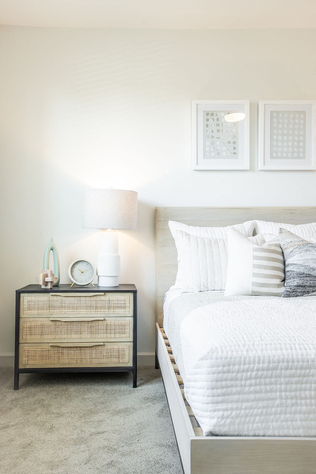 a white bedroom with a bed and a nightstand with a lamp and pictures on