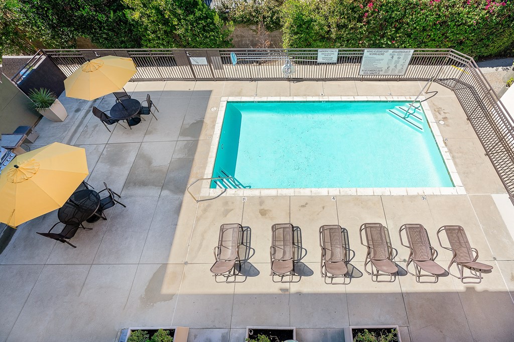 an aerial view of a pool with chairs and umbrellas