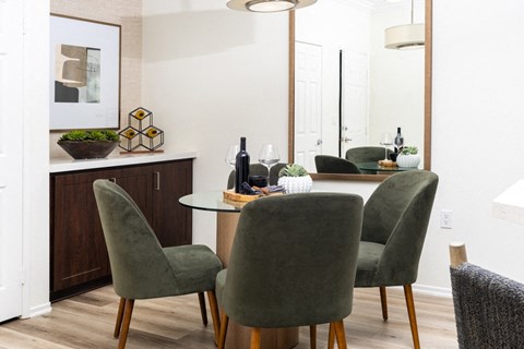 Dining nook with a round glass table, green velvet chairs, a tall framed mirror, and a dark wood buffet cabinet.