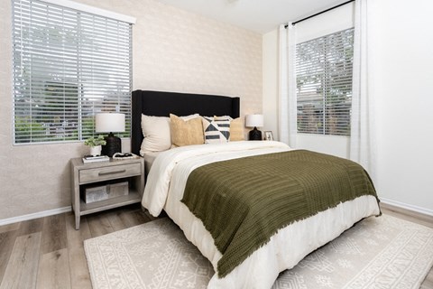 Bedroom with a black upholstered headboard, a patterned accent wall, two blinded windows, and a wood nightstand.