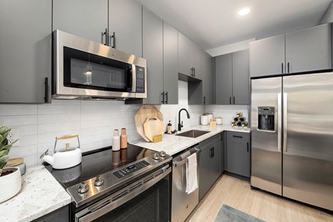 Kitchen with gray cabinets, granite counters, subway tile, and a stainless run including a side-by-side refrigerator.
