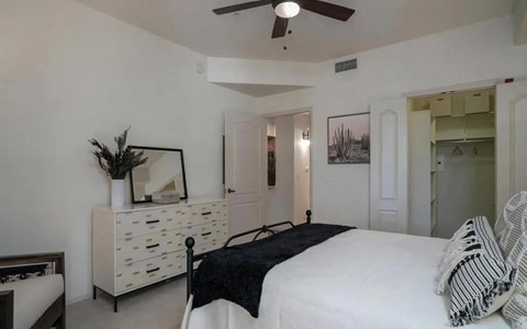 Carpeted bedroom with a ceiling fan, a dresser and mirror, and an open closet with shelving and a hanging rail.