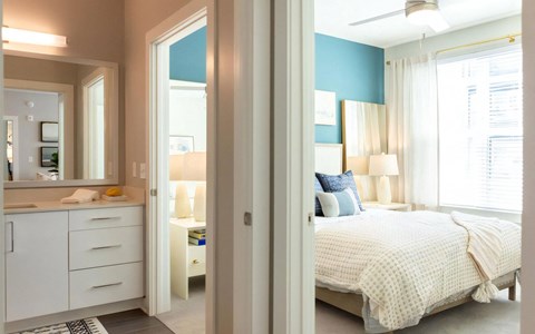 Bathroom vanity in the foreground with a doorway through to a bedroom with a teal accent wall and a ceiling fan.