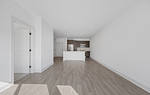 Vacant open living area with wood-look plank flooring, looking the length of the room toward the kitchen island.