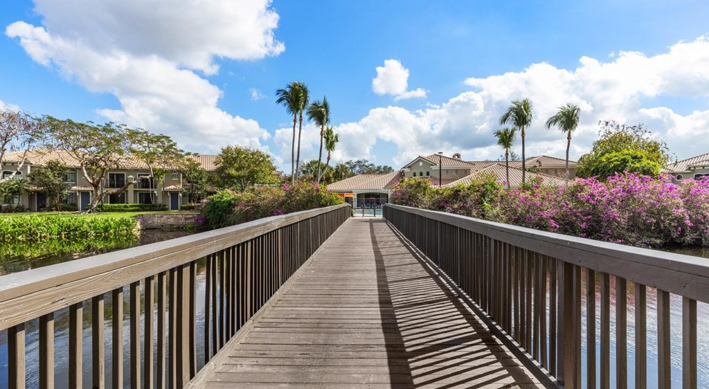 A wooden walkway leads to a row of houses with a blue sky and clouds in the background.