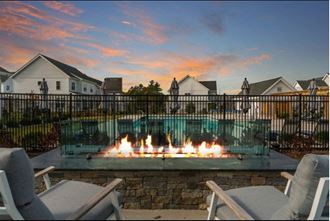 a pool with a fire pit in front of a house with a sunset in the background