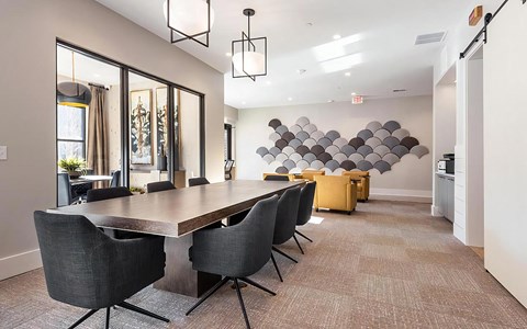 Communal work space with a long wood table, eight swivel chairs, pendant lights, and a scalloped wall installation.