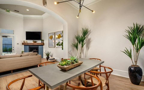 Clubroom dining area with a gray table, wood chairs, sputnik chandelier, and a tiled fireplace with a television above.