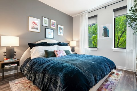 Bedroom with a framed gallery wall, upholstered headboard and two tall windows looking into leafy tree canopy.