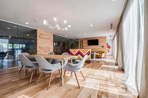 Clubroom dining table for eight under a globe chandelier, with a wall television and lounge seating beyond it.