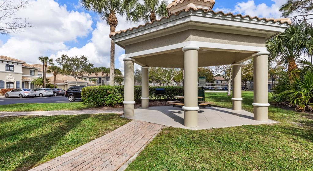 A gazebo with a tiled roof is surrounded by a grassy area and a brick walkway.